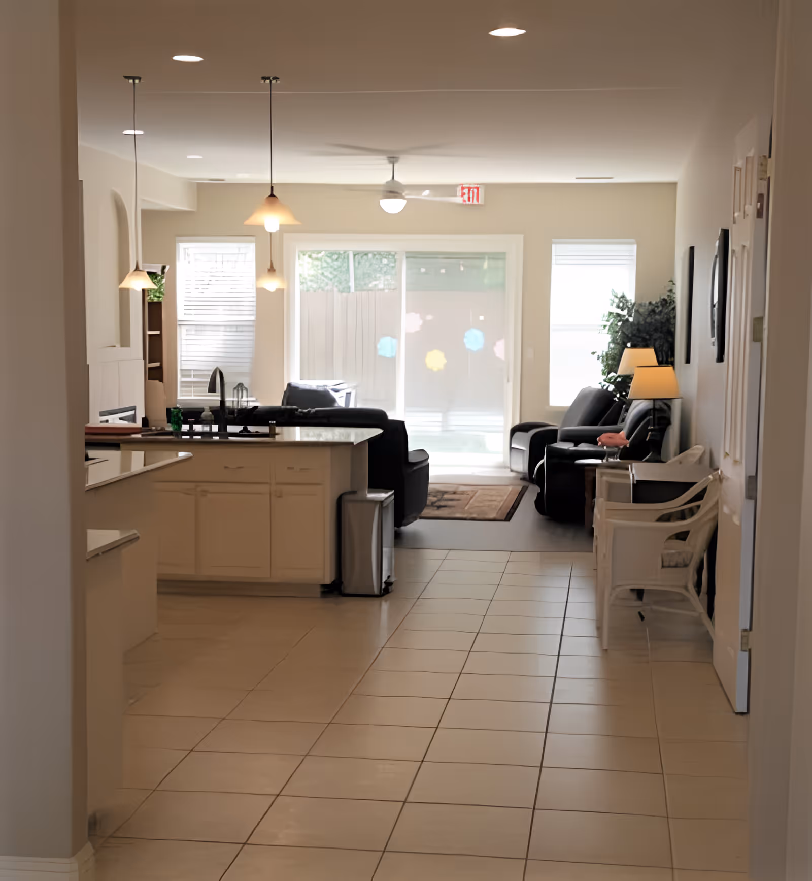 Open-plan interior showing a kitchen island leading into a living room with armchairs and a sliding glass door.