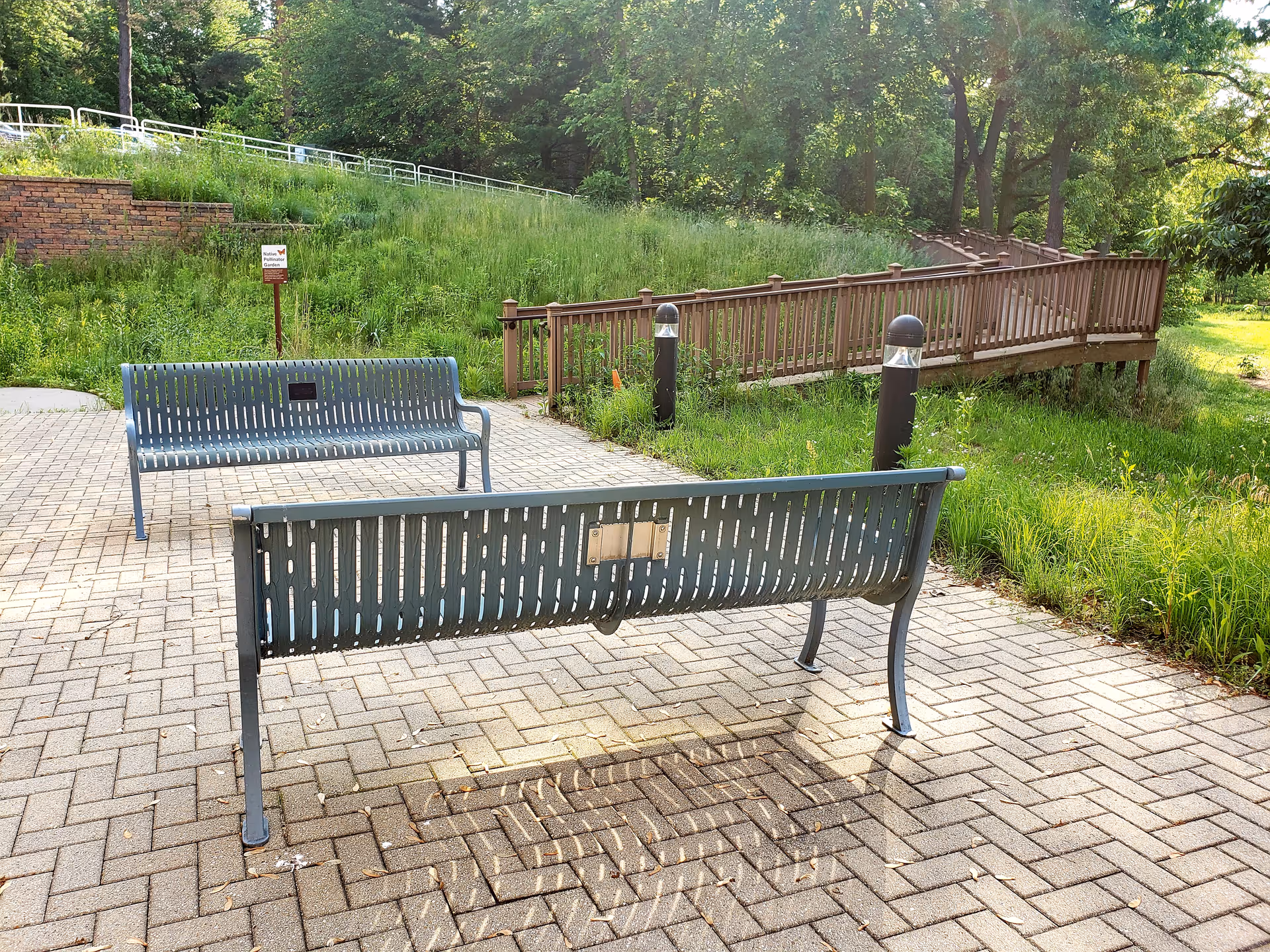 Two metal benches on a paved patio area with a wooden ramp and green grassy area with trees in the background at Catherine Kasper Life Center.