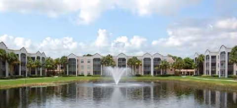 Front view of Brookdale West Palm Beach with a fountain pond and palm trees.