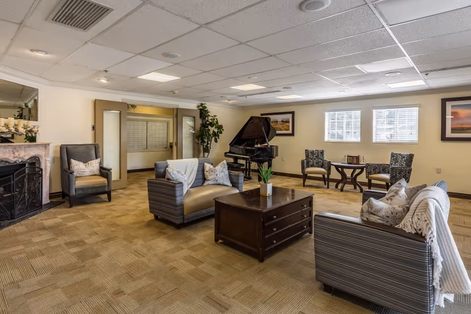 Spacious lounge with sofas, armchairs, a grand piano and coffee table in a senior living facility.