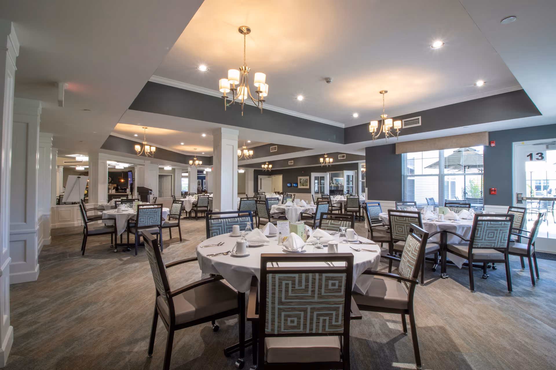 Spacious dining room with round tables set with white tablecloths and chairs under chandeliers.
