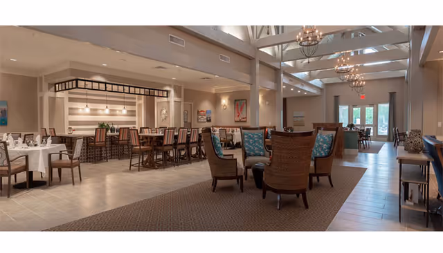 Spacious dining and lounge area with tables, bar seating, and wicker armchairs under exposed beam ceilings and chandeliers.