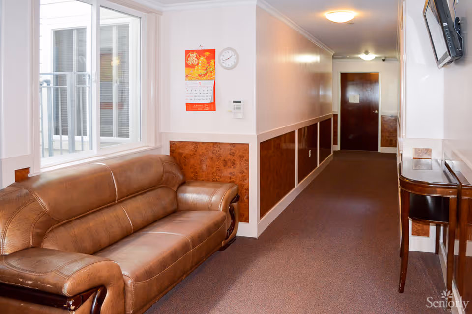 A hallway in Merced Residential Care featuring a leather sofa, wall calendar, and door at the end.