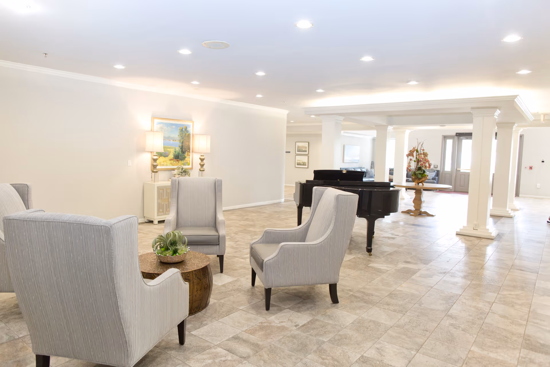 Spacious bright lobby with a seating area of upholstered chairs, a grand piano, columns and a tiled floor.