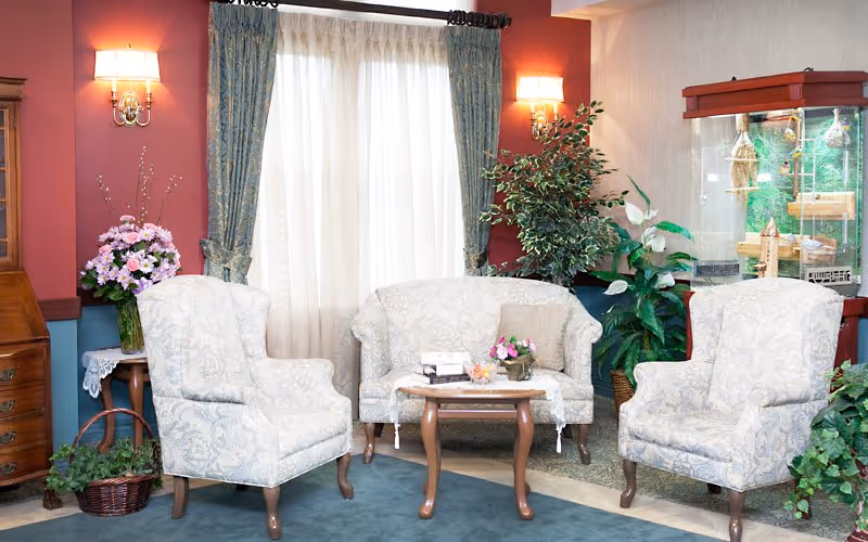 Cozy living room lounge with four patterned chairs around a coffee table, plants and curtains.