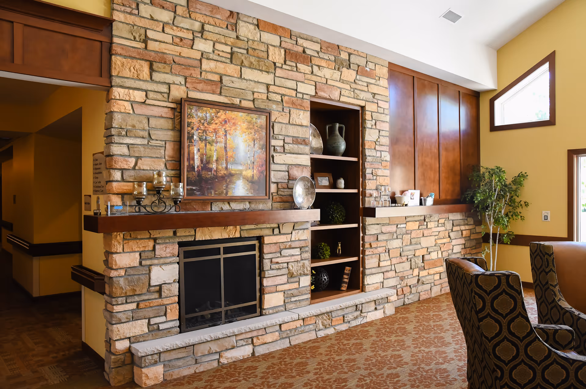 Cozy communal living room with a stone fireplace, built-in shelving, decorative accents, and upholstered chairs.