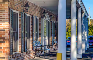 Exterior of Marquis Centennial Post Acute Rehab building featuring brick walls, shutters, and benches.