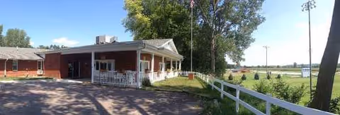 Elms Health Care Center's red brick building with a white porch beside a rural driveway