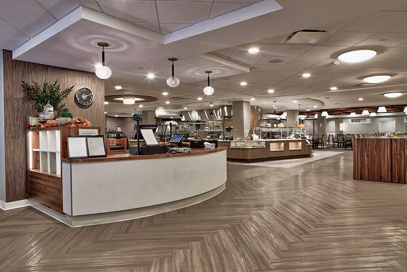 Spacious modern dining and serving area with a curved reception counter, buffet stations, and seating under pendant and recessed lighting.