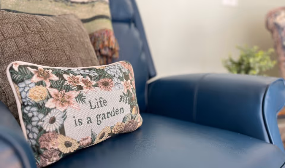 Decorative floral pillow reading 'Life is a garden' resting on a blue leather chair in a cozy seating area.
