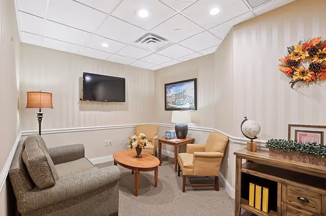 Small comfortable sitting room with a sofa, two armchairs, coffee table, wall-mounted TV and decorative accents.