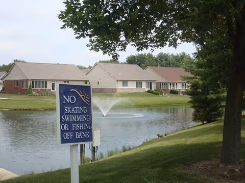 A pond with fountain, grassy bank, and single-story townhomes in the background.