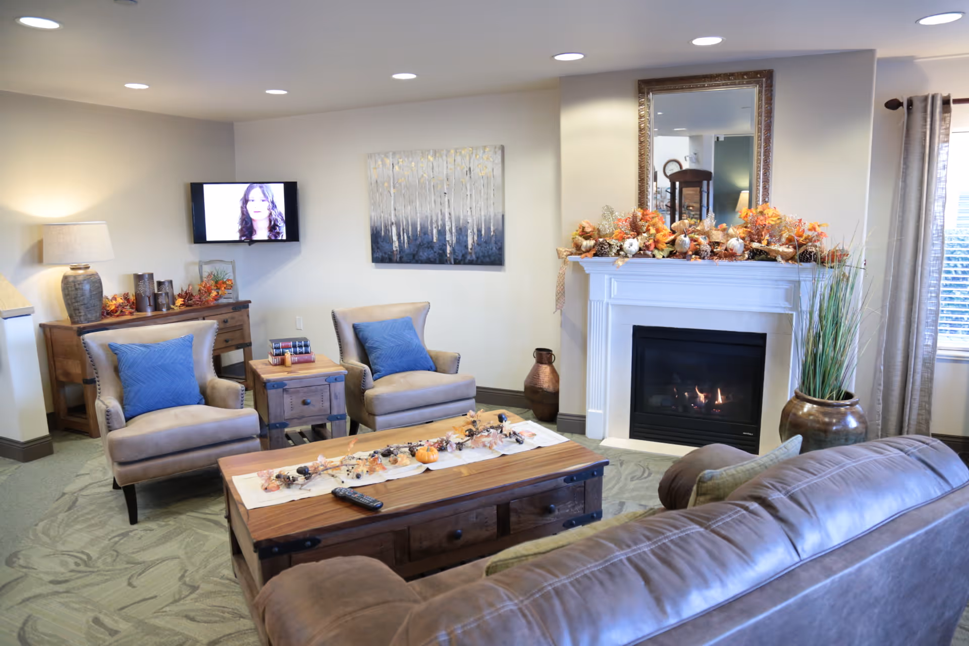Comfortable living room with a sofa, two armchairs, a coffee table, a fireplace decorated for fall, and a wall-mounted TV.
