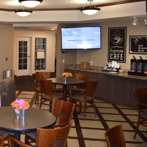 Small café-style common area with round tables and chairs, a coffee station, and a wall-mounted TV.