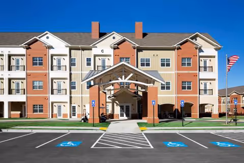 Three-story senior living building with a central covered entrance and wheelchair-accessible parking.