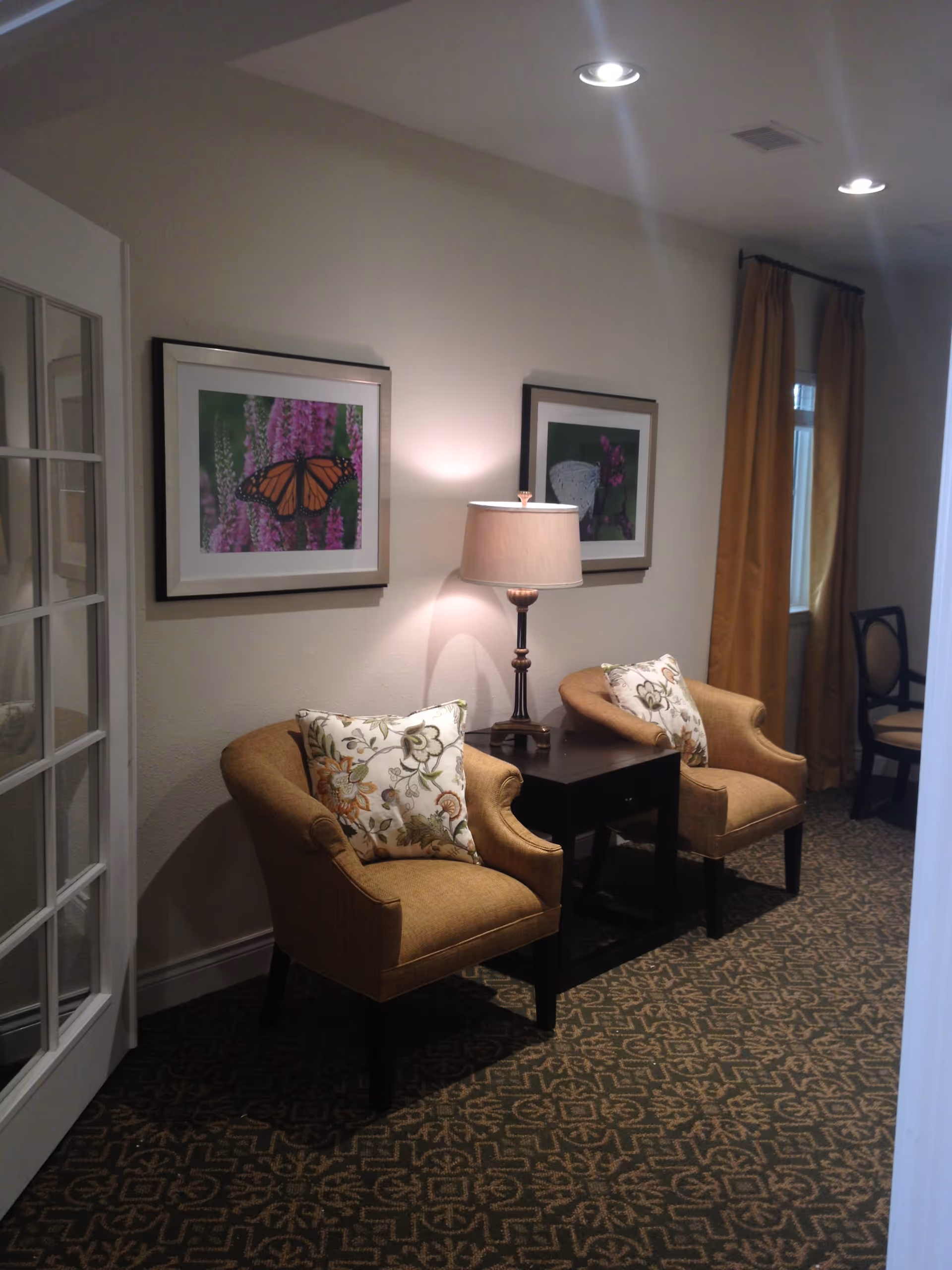 A cozy seating area with two upholstered armchairs, a side table with a lamp, and framed artwork on the wall.