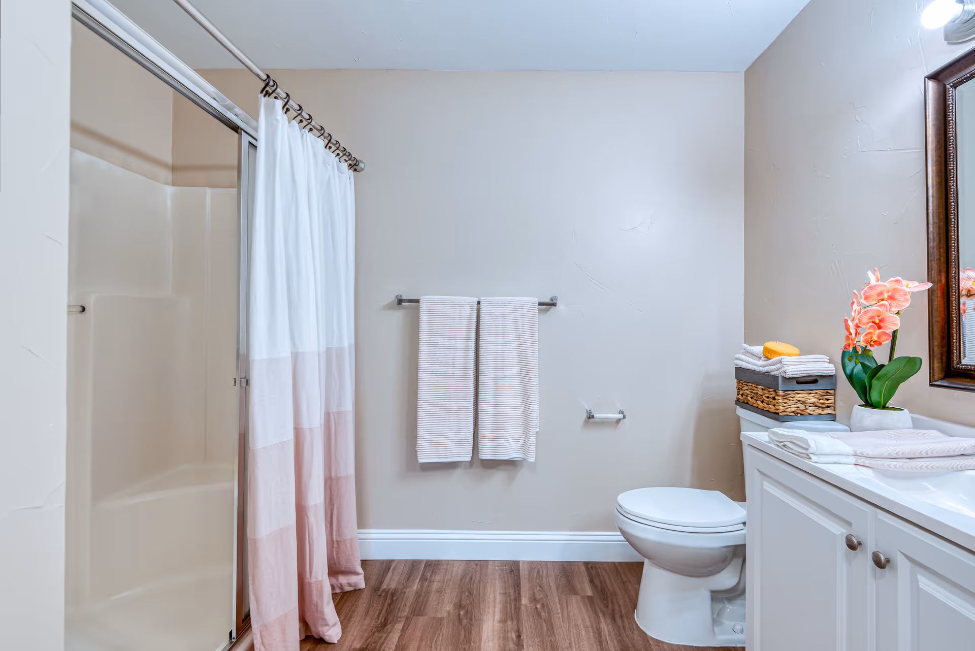 A clean bathroom with a shower and curtain, toilet, vanity with mirror, towels, and a potted flower.