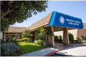 Entrance of Anaheim Terrace Care Center with a blue awning displaying the facility name, surrounded by greenery and a tree on the left side.