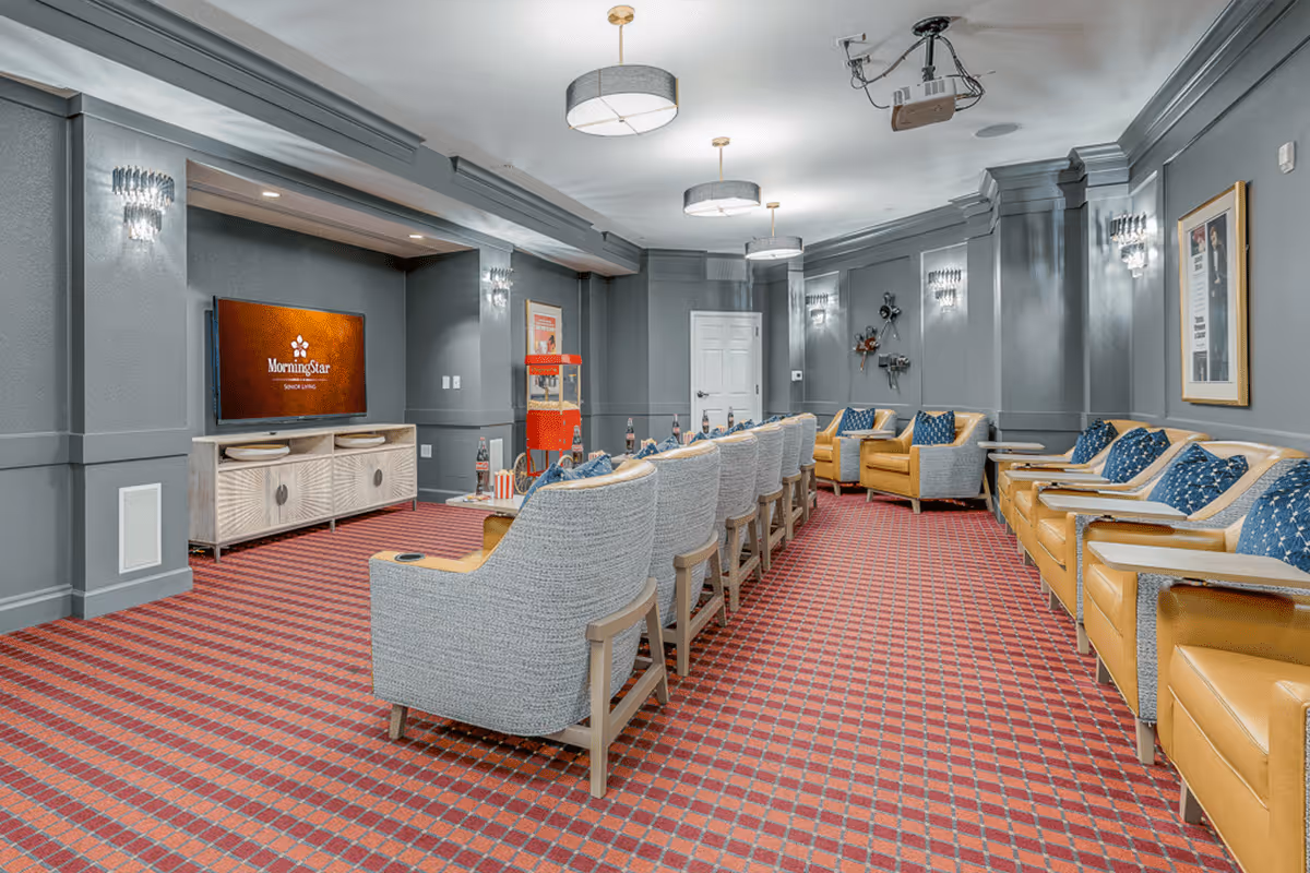 Carpeted screening room with rows of upholstered armchairs facing a wall-mounted TV and a popcorn machine.