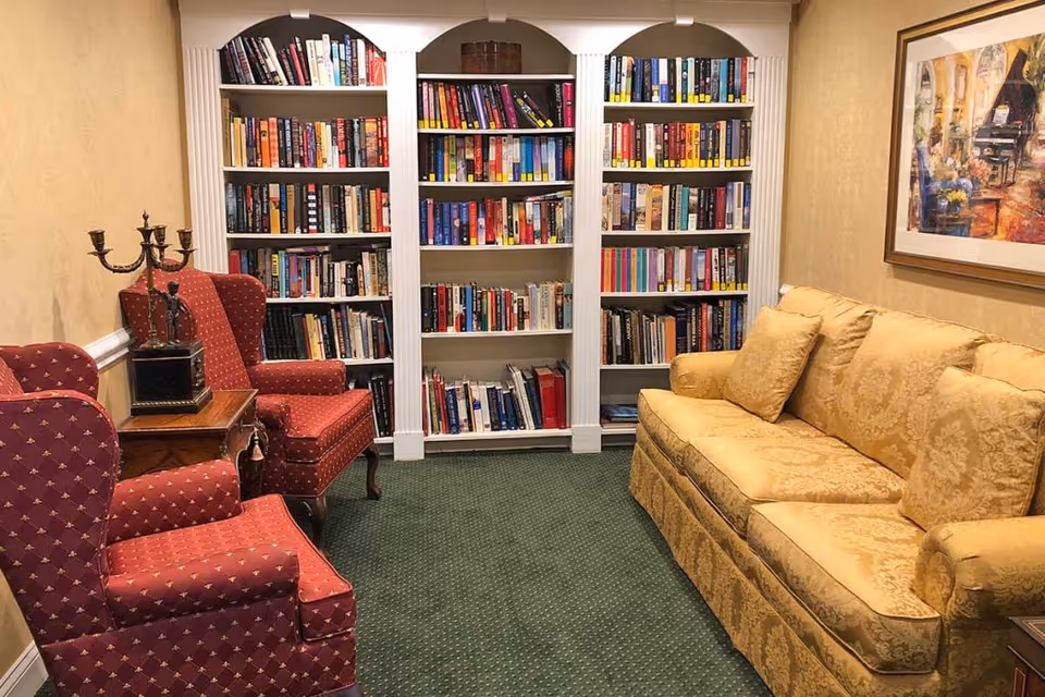 Cozy reading room with built-in white bookshelves, two red upholstered armchairs, and a yellow patterned sofa on green carpet.