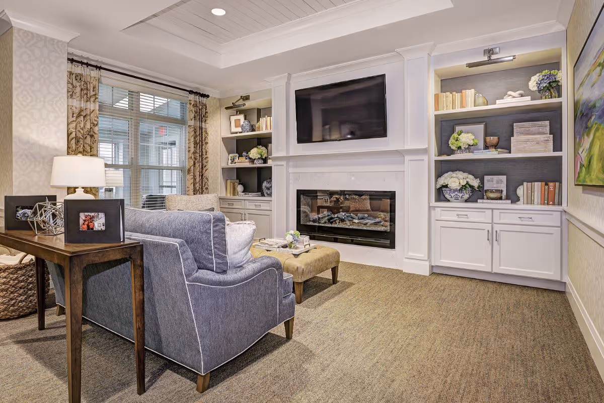 Comfortable living room with a sofa, ottoman, wall-mounted TV above a fireplace, and built-in shelving.