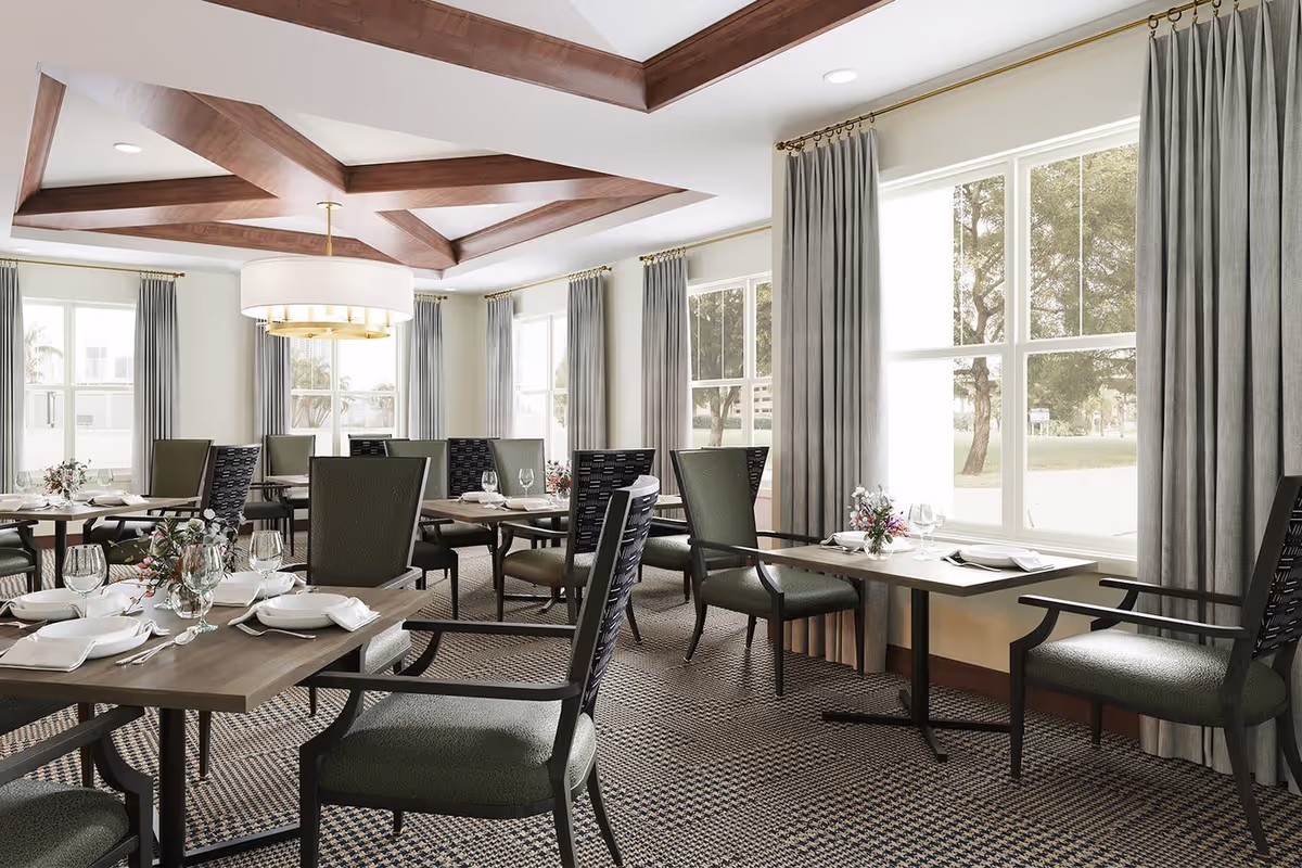 Bright dining room with multiple set tables and chairs, large windows with curtains, and decorative wooden ceiling beams.