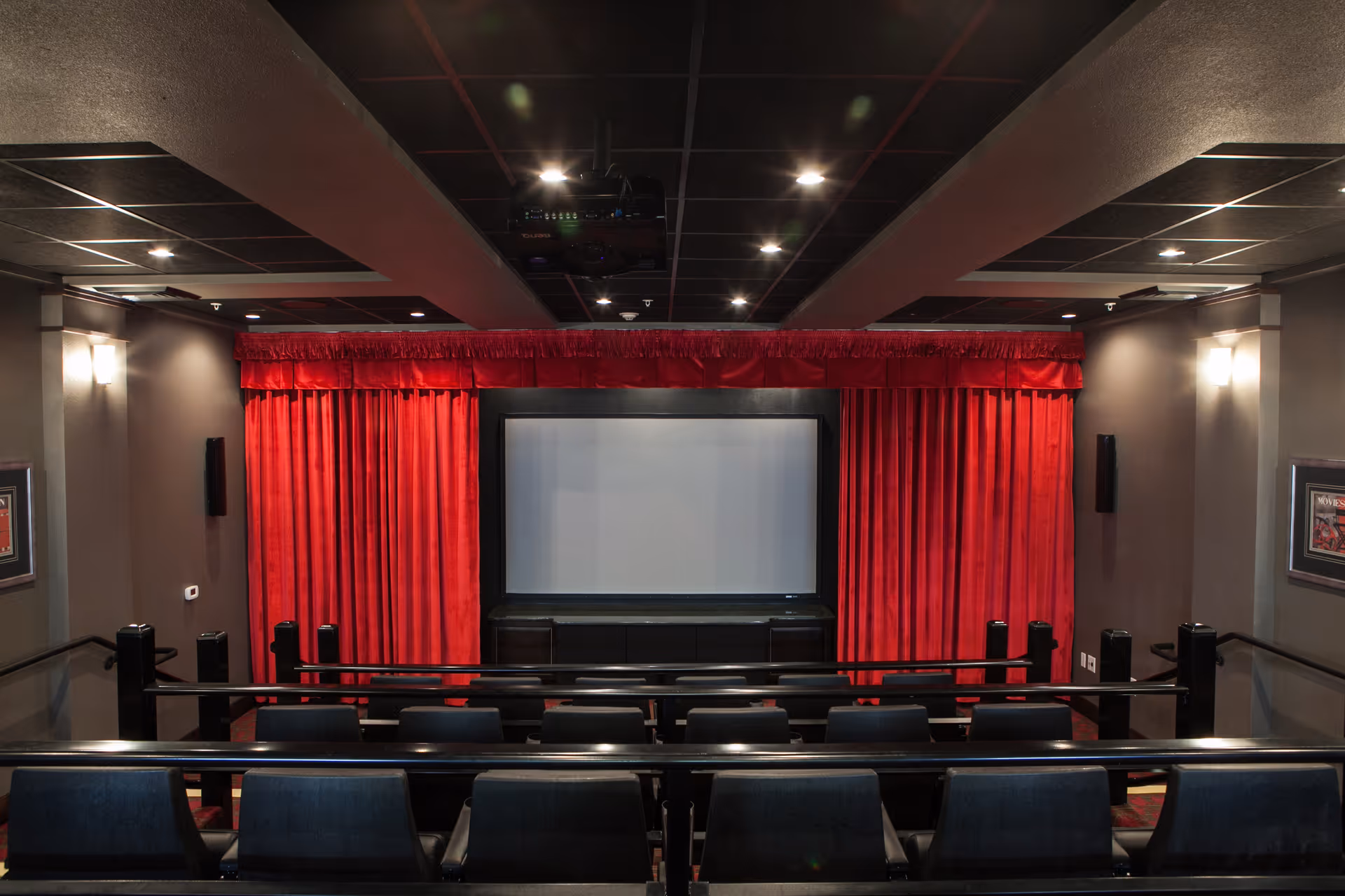 Small indoor movie theater with rows of seats facing a screen framed by red curtains.