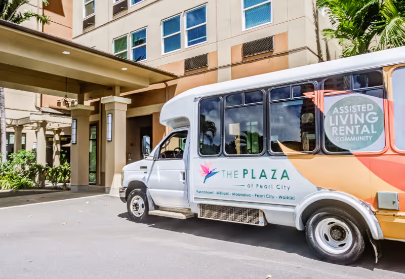 A shuttle bus for The Plaza at Pearl City parked in front of the facility entrance.
