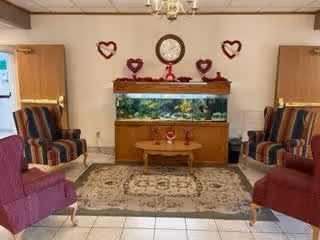 Comfortable sitting area with an aquarium centered between upholstered armchairs, a small coffee table on a rug, and heart decorations on the wall.