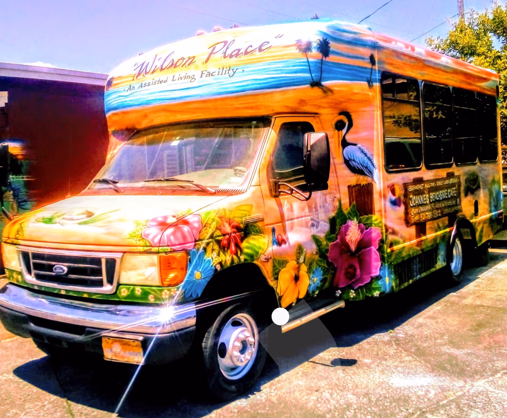 Colorfully painted Wilson Place assisted living shuttle bus with floral and bird murals parked outdoors.
