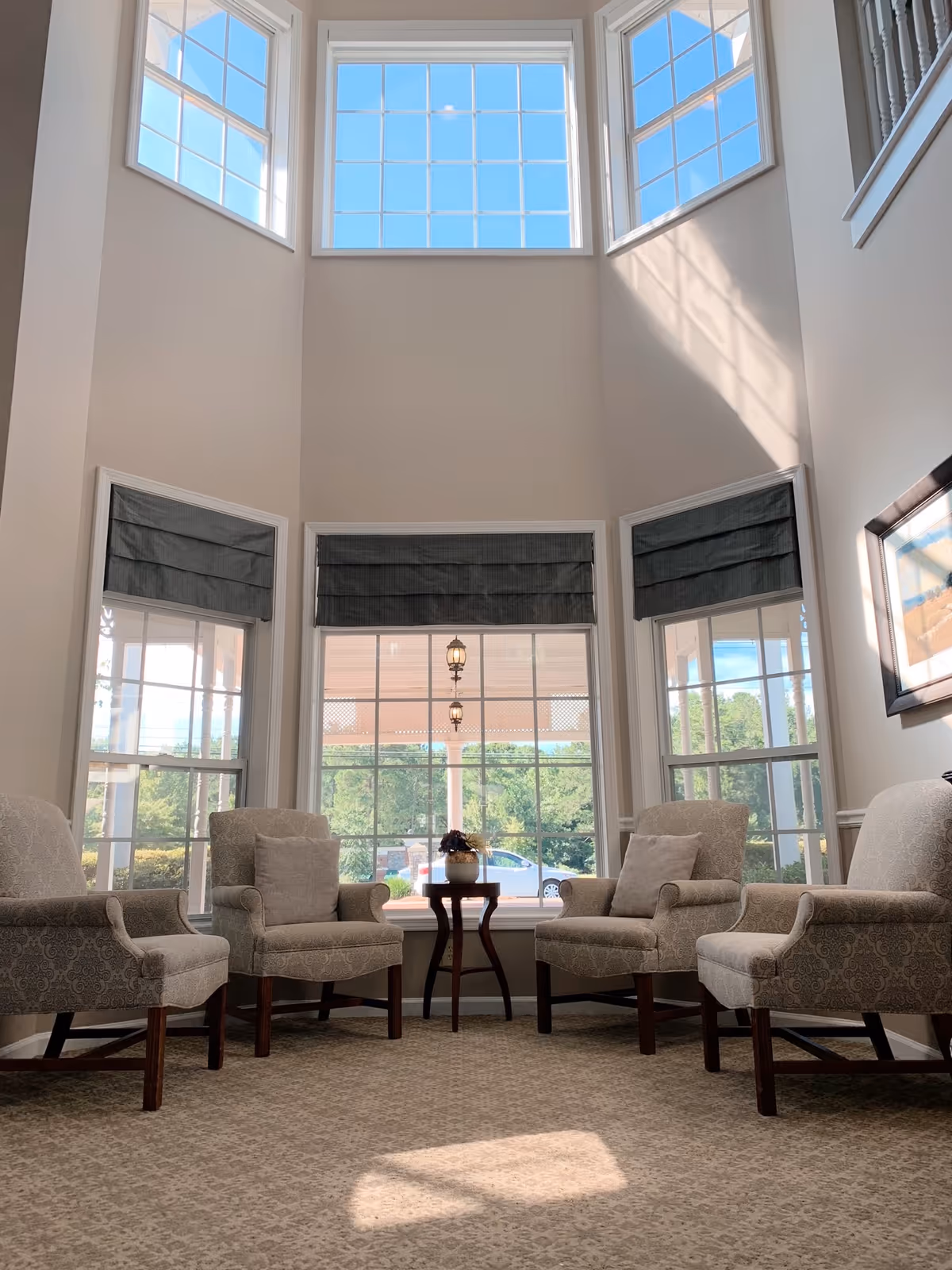 Sunlit seating area with four upholstered armchairs arranged around a small table in front of tall multi-pane windows.