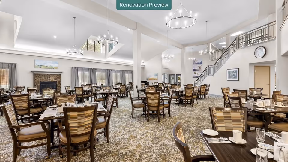 Spacious dining room with multiple set tables and patterned chairs, chandeliers, and a staircase in the background.