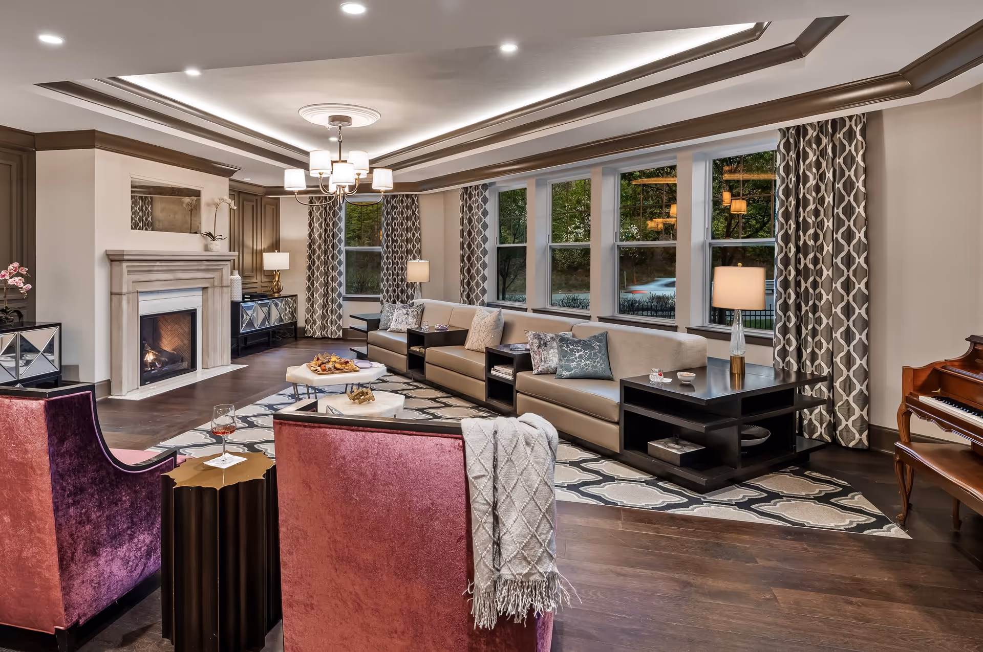 Spacious, elegantly furnished common living room with a fireplace, sofa seating, armchairs, large windows, and a piano.