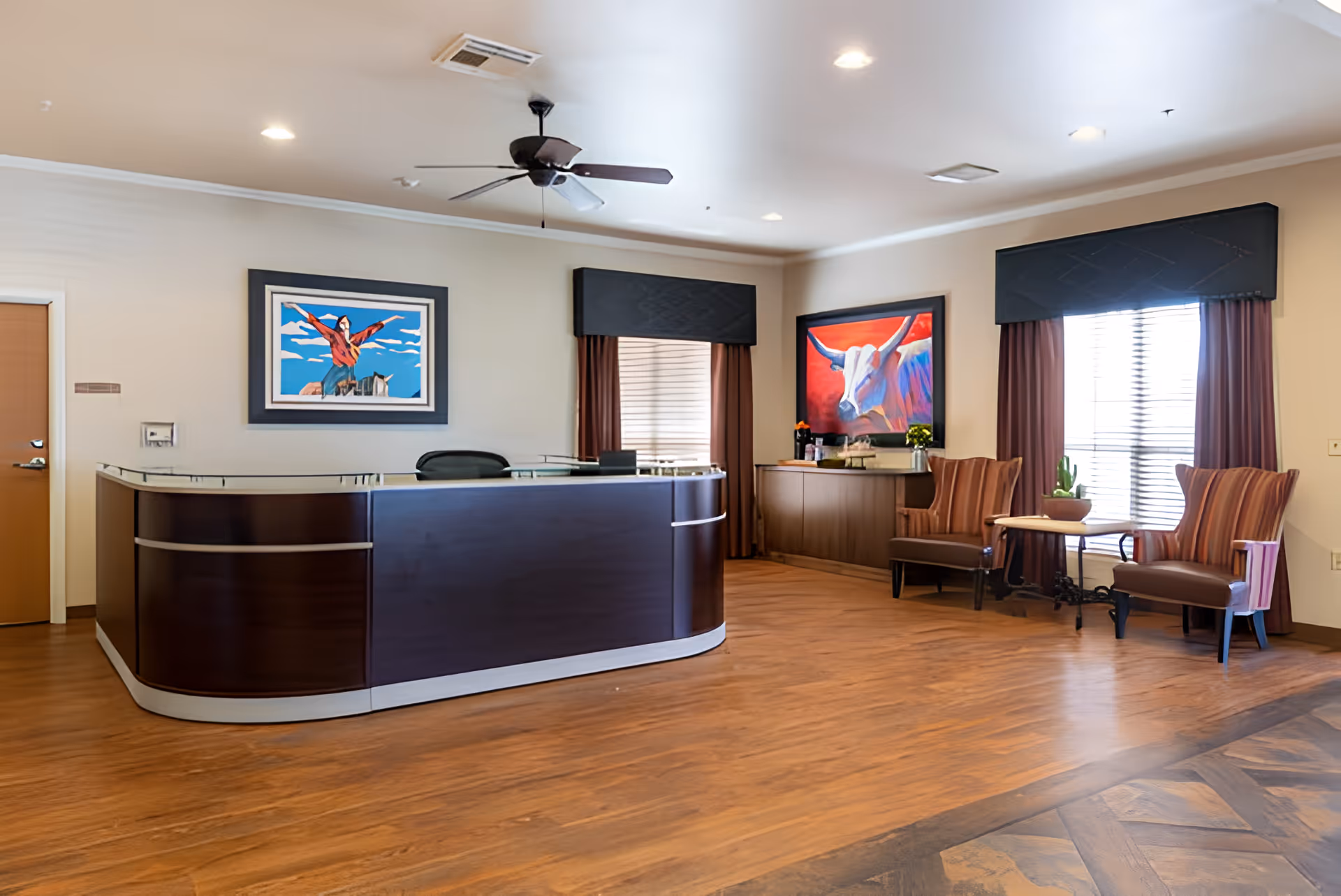 Reception area with a curved wooden front desk, seating chairs, colorful artwork on the walls, and wood flooring.