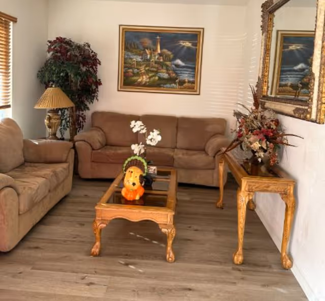 Cozy living room in a residential care facility with beige couches, coffee table, and artwork.