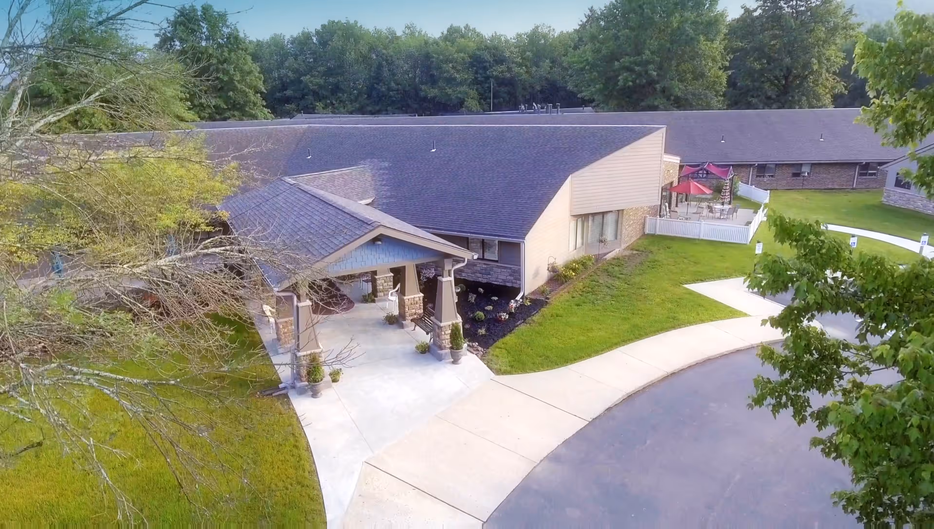 Aerial view of Warren Manor showing the covered entrance/porte-cochere, curved driveway, walkways, patio area, and surrounding trees and lawn.