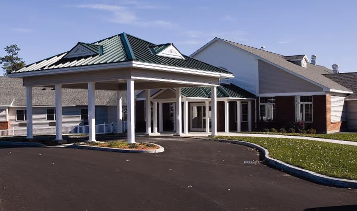 Front entrance of a single-story senior living building with a covered porte-cochère and paved driveway.