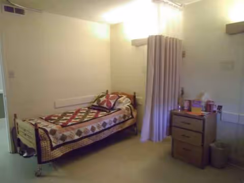 Single bed with quilt, curtained area, and dresser in a senior facility bedroom.