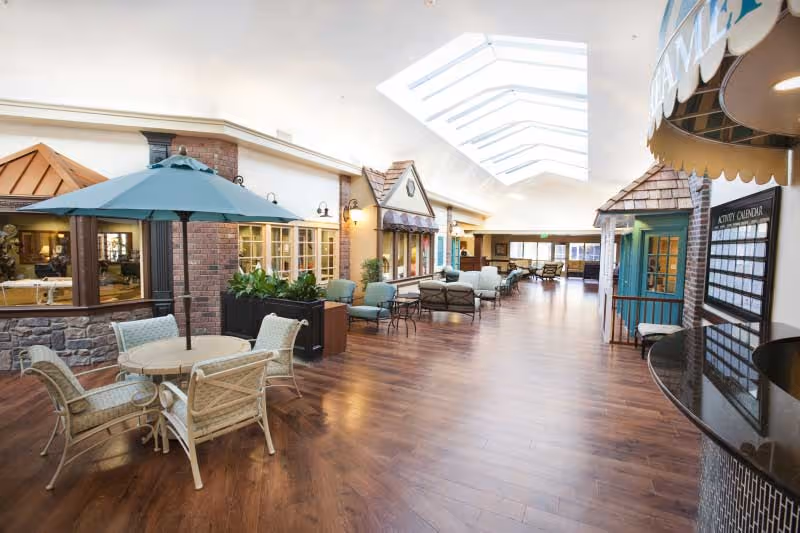 Bright indoor communal area with wood floors, skylights, cafe-style seating and small storefront facades forming a simulated main street.