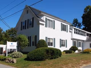 White two-story senior living building with manicured shrubs and an Arbor Terrace sign.
