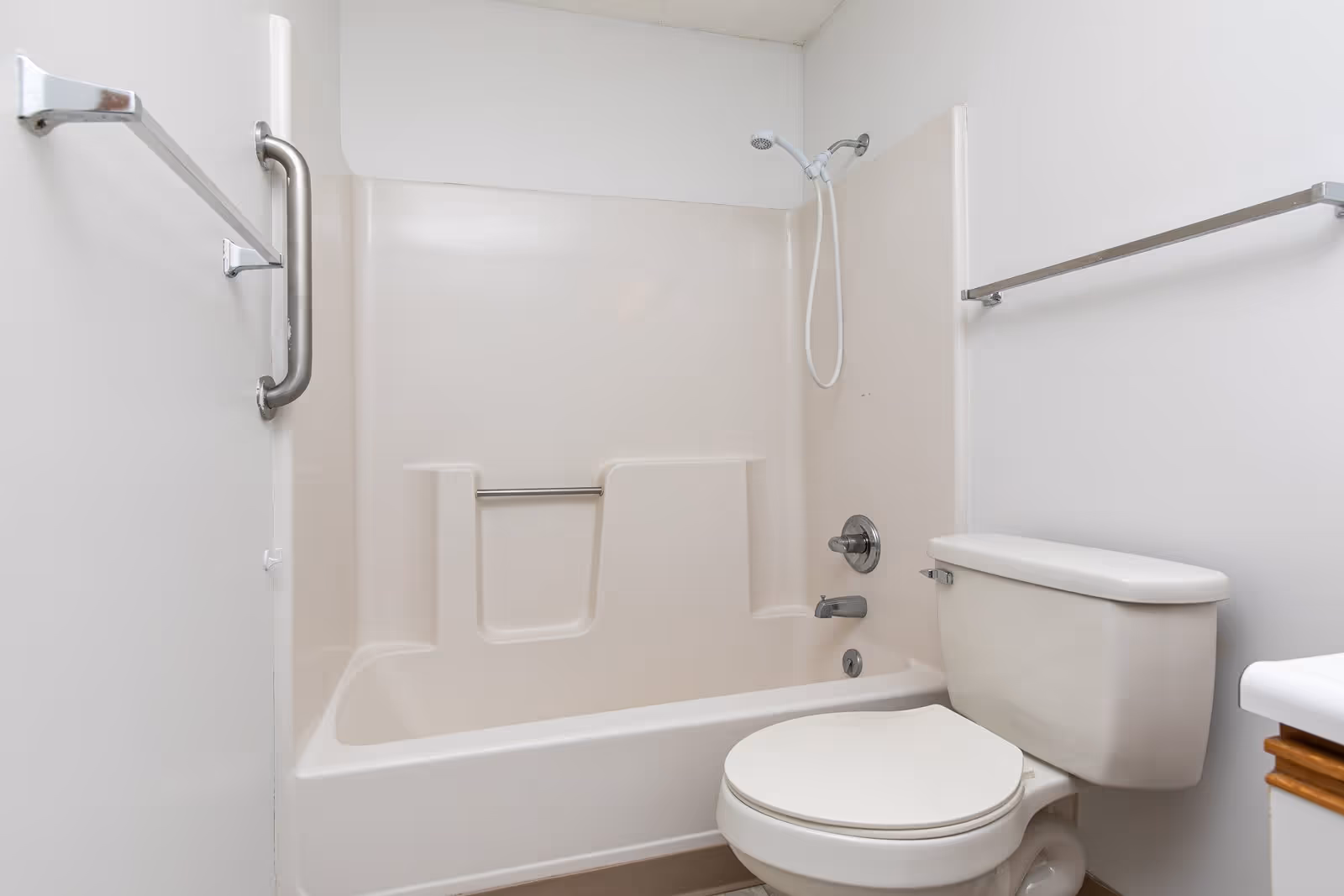 Bathroom featuring a bathtub/shower combination with a handheld showerhead, grab bar, towel rails, and a toilet.