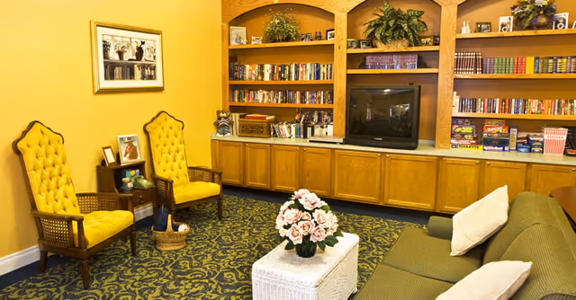 Cozy sitting room with built-in bookshelves and a TV, two yellow tufted chairs, a green sofa, and a small coffee table topped with pink flowers.