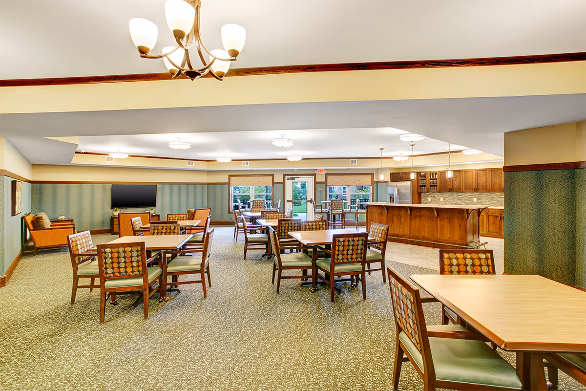 A spacious dining and common area with multiple tables and chairs, a TV, and a wooden kitchenette/bar.
