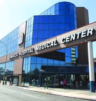 Sunlit glass-front hospital exterior featuring Jamaica Hospital Medical Center signage and main entrance.