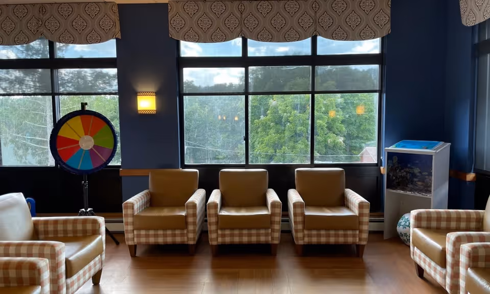 Several patterned armchairs arranged in front of large windows with a colorful prize wheel to the left.
