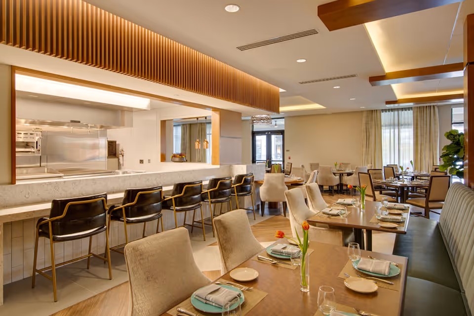 Bright modern dining room with set tables, a marble counter with bar stools and an open kitchen in the background.