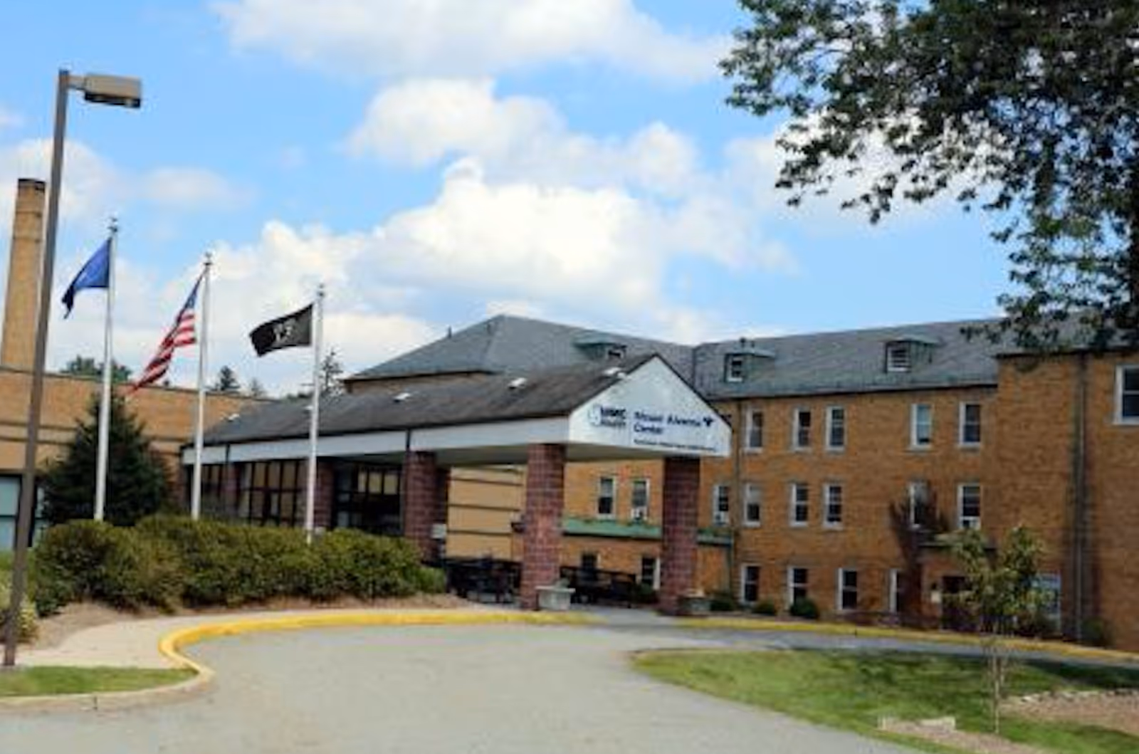 The exterior entrance of the Mt Alverno Center senior living facility, featuring flags and a landscaped path.