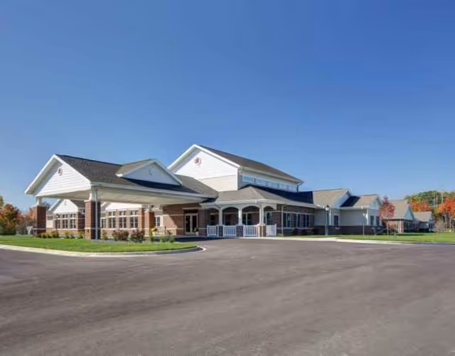 Exterior view of a modern senior living facility with a curved entrance and parking lot.