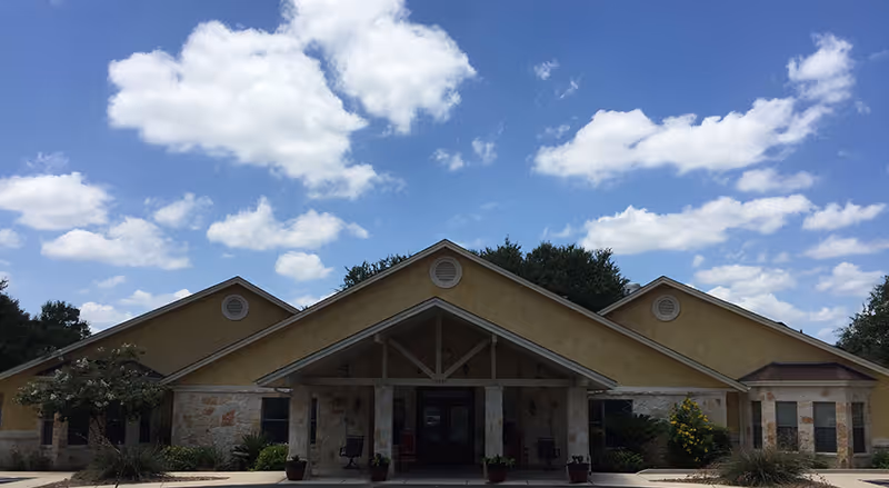 Front exterior of a single-story stucco and stone building with a covered gabled entrance under a blue sky.