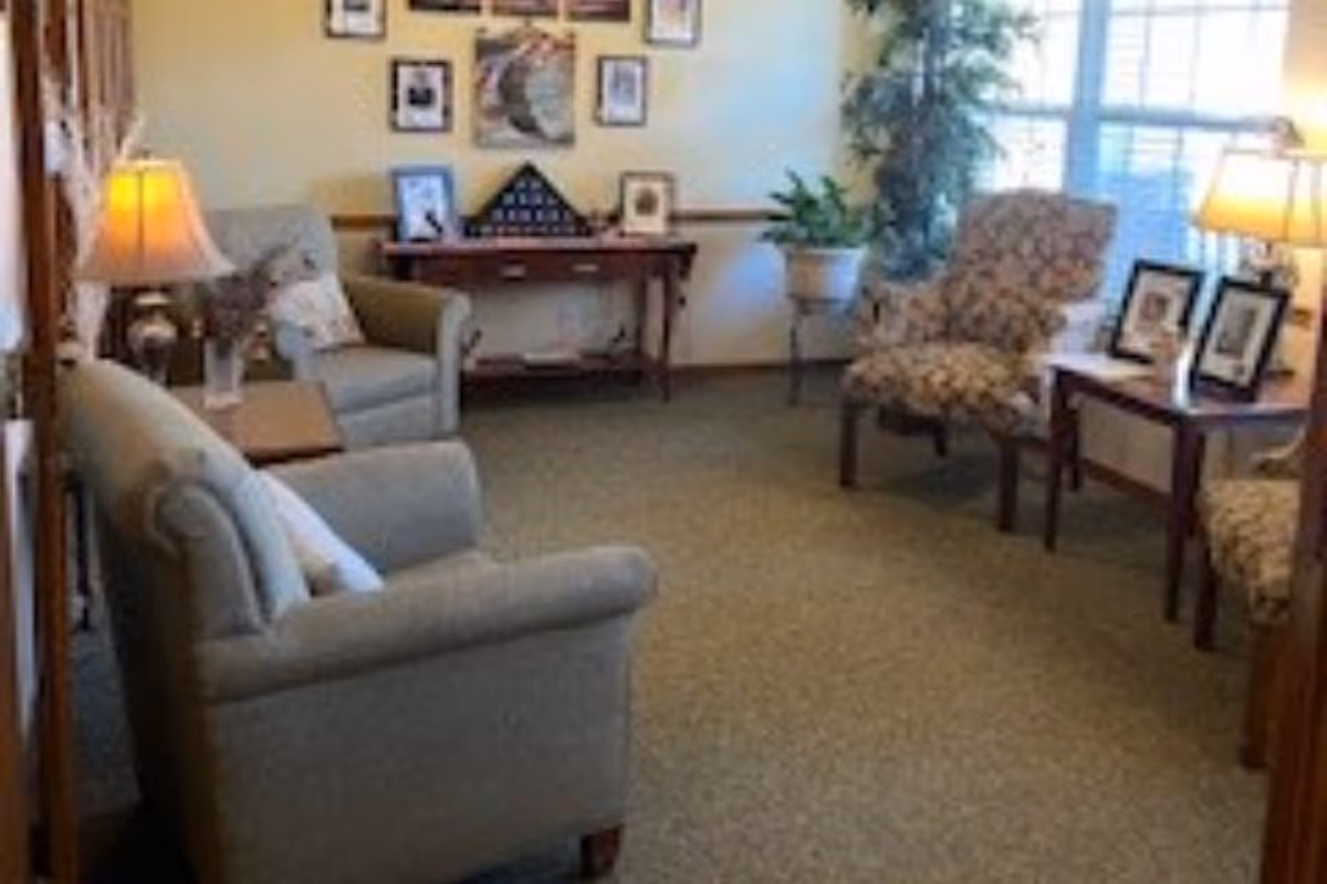 Cozy seating area with sofas and armchairs, side tables with lamps and framed photos by a large window.